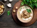 Aksamitna zupa grzybowa z pieczarek, udekorowana śmietaną i natką, podana z grzankami.