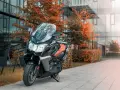 Skuter BMW C650 GT z brązowym siedzeniem na tle nowoczesnego budynku i jesiennych drzew. Dane techniczne tego modelu są imponujące.