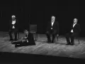 Czterech aktorów w garniturach na scenie. Jeden siedzi na podłodze, pozostali na krzesłach. Kwartet dla czterech aktorów.