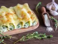 Złociste cannelloni ze szpinakiem, zapieczone pod ciągnącym serem, prezentują się apetycznie na drewnianej desce.
