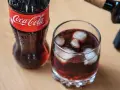 Szklanka z lodem i napojem, obok butelka Coca-Coli. Idealne na gorący dzień, gdy masz ochotę na wino z colą.