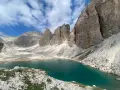 Il **lago di Antermoia**, incastonato tra imponenti vette rocciose, riflette il cielo azzurro e le nuvole bianche. Un gioiello alpino.