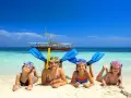 Cztery uśmiechnięte dzieci w maskach do snorkelingu i płetwach leżą na plaży. W tle turkusowa woda i łódź. Idealny dzień, kiedy na Zanzibar!