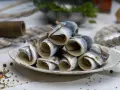 Gestapelte Rollmops Fisch auf einem Teller, garniert mit Gewürzen und Holzspießen.