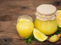 Due vasetti di marmellata di limoni, limoni freschi e foglie di menta su un tavolo di legno.