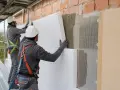 Operai in cantiere applicano pannelli isolanti per forare cappotto termico. Lavori di isolamento esterno.