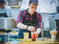 Ein junger Mann, der als Werkstudent 20 Stunden pro Woche arbeitet, mixt Getränke in einem Streetfood-Laden.