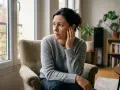 Femme assise près d'une fenêtre, le regard perdu, une main sur l'oreille comme pour entendre un bip dans l'oreille.