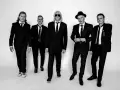Fünf Männer in schwarzen Anzügen und Krawatten, die wie der titel von Def Leppard aussehen, posieren für ein Schwarz-Weiß-Foto.