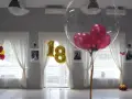 Złote balony z cyfrą 18 i przezroczyste balony z różowymi w środku ozdabiają salę. Balony na stołach tworzą radosną atmosferę.