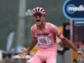 Isaac Del Toro, a cyclist in a pink jersey, screams in triumph, arms outstretched.