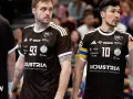 Dwóch zawodników w brązowych koszulkach, jeden z numerem 93, drugi z numerem 10. Luka Cindrić, kapitan z opaską na ramieniu, rozmawia z kolegą z drużyny.