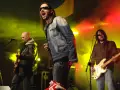Energetyczne kapele punkowe z lat 80. na scenie, w dymie i kolorowych światłach. Wokalista krzyczy do mikrofonu, gitarzysta gra na basie.