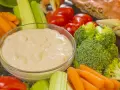 Un bol de sauce crudités crème fraîche entouré de carottes, céleri, tomates cerises et brocolis. Un crabe cuit est visible en arrière-plan.
