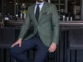 Elegancki mężczyzna w marynarce w kratę (butelkowa zieleń) i granatowych spodniach. W tle bar z elementami pudrowego różu.
