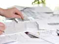 Mano calculando y anotando en libreta, rodeado de papeles y facturas con retención.