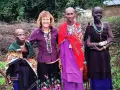 Uśmiechnięta kobieta z Europy wśród ludności Tanzanii. Trzy kobiety z plemienia Masajów w tradycyjnych strojach i biżuterii.