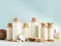 Butelki z mlekiem roślinnym (kokosowym, migdałowym, owsianym) dla osób z uczuleniem na laktozę. Obok składniki: kokos, migdały, płatki owsiane, ryż.