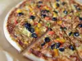 Co to jest pizza? To pyszna, okrągła pizza z oliwkami, papryką i serem, pokrojona na kawałki.