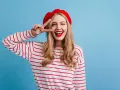 Mujer con boina roja y camiseta a rayas, haciendo el signo de la paz, con un estilo que evoca un caracter francés.