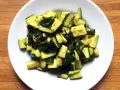 Zucchine in umido, un contorno saporito e leggero, servito in un piatto bianco su un tagliere di legno.
