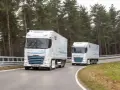 Dwa białe elektryczne DAF XG Plus z naczepami jadące po krętej drodze wśród drzew.