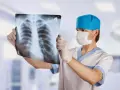 Un radiologo con mascherina e guanti esamina una radiografia del torace, analizzando attentamente ogni dettaglio per una diagnosi accurata.