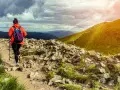 Kobieta w pomarańczowej kurtce wyrusza na szlak. To prawdziwy hiking po polsku, z pięknymi widokami i kamienistą ścieżką.