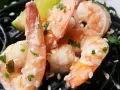 Krewetki z czarnym makaronem, posypane sezamem i natką pietruszki, z kawałkiem limonki.