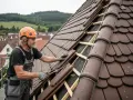 Handwerker mit Helm legt Ziegel auf ein Dach. Er ist dabei, das Dach zu beschichten und sorgt für Schutz vor Wind und Wetter.