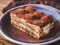 Pyszny kawałek tiramisu z mascarpone, posypany kakao, na niebieskim talerzu. Idealny na deser.