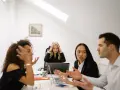 Un gruppo di colleghi di lavoro discute animatamente. Una donna bionda sembra stressata, tenendosi la testa tra le mani.