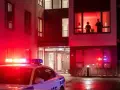Radiowóz policyjny z włączonymi sygnałami świetlnymi przed budynkiem mieszkalnym. W oknie widać sylwetki ludzi, być może naruszających ciszę nocną w Polsce.