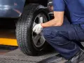 Mechanik w białych rękawiczkach dokręca śruby koła. Czas pomyśleć, kiedy wymienić opony na letnie.