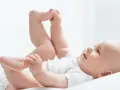 Uśmiechnięte dziecko leży na plecach, podnosząc nóżki. Czas na zmianę pampersów na większe, gdy maluch rośnie.