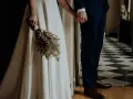 Para młoda trzyma się za ręce, ona z bukietem suszonych kwiatów. Wesele motywy w eleganckim wnętrzu.