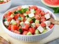 Erfrischender **Salat mit Melone**, Gurke und Feta in einer weißen Schüssel, garniert mit Minze. Perfekt für heiße Tage.