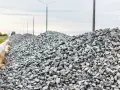Stos kruszywa, idealnego jako składnik betonu B25, na tle słupów oświetleniowych i nieba.