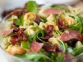 Sałatka z tortellini, suszonymi pomidorami, rukolą i salami w szklanej misce.