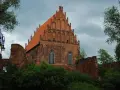 Gotycka ceglana budowla z pomarańczowym dachem, otoczona zielenią i fragmentami murów. Widok na Elbląg, województwo warmińsko-mazurskie.