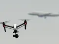 A white drone with red lights hovers in the sky, possibly on a security mission, as a blurred airplane flies in the distance.