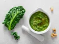 Pesto z jarmużu do słoika, gotowe do przechowywania. Obok liść jarmużu i orzechy nerkowca.