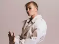Rosalie, piosenkarka, w beżowym płaszczu i z ozdobą na nosie, prezentuje swoje dłonie z pierścionkami.