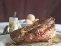Costilla de ternera asada jugosa con hueso, servida en plato blanco con salsa y guarnición.