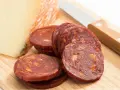 Plasterki pikantnego chorizo, kawałek sera i nóż na desce. Idealne na przekąskę, zastanawiasz się chorizo co to?