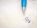 Niebieski długopis nad plamą z atramentu na jasnym materiale. Dowiedz się, jak usunąć pieczątkę z papieru, gdy zdarzy się wypadek.