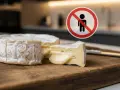Un camembert coupé sur une planche en bois, avec un panneau d'interdiction. Question : quel fromage manger enceinte ?