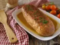 Polpettone in padella dorato, guarnito con erba cipollina, servito su un piatto bianco con salsa. Accanto, una spatola di legno e pomodorini.
