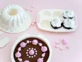 Förberedelser för ett härligt baka kalas! En sockerkaksform, muffinsform och en färdig chokladkaka med rosa maränger och strössel.