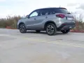 Szary Suzuki Vitara Hybrid z czarnym dachem stoi na betonowej nawierzchni z żółtymi pasami.